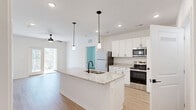 Located at 660 Aubrey Ln in Calabash, NC, this well-designed 2-bedroom, 2-bathroom single-floor home offers a clean, modern aesthetic throughout. The open-concept living area seamlessly connects the living room, dining space, and kitchen, all bathed in natural light and finished with light-toned hardwood-style flooring. A ceiling fan anchors the living area, which opens to a private outdoor deck with wood railing, framed by lush wooded views.

The kitchen is a standout feature, centered around a large granite island with a double undermount sink and matte black faucet, illuminated by sleek pendant lighting. White shaker-style cabinetry lines the walls, complemented by granite countertops and a full suite of stainless steel appliances, including a range, microwave, and refrigerator. A pantry provides additional storage convenience.

Both bedrooms are bright and airy, with large windows overlooking the surrounding tree canopy and ceiling fans for comfort. The primary bedroom includes a walk-in closet with wire shelving. The two bathrooms are finished in a consistent modern style, featuring white vanities, black hardware accents, large mirrors, and light wood-look flooring. One bathroom offers a tub-shower combo, while the other features a walk-in shower. A dedicated laundry area and utility room round out this efficiently organized home.