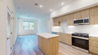 Located at 1205 Aviara Parkway in Carlsbad, CA, this thoughtfully designed 2-bedroom, 1-bathroom residence offers a clean, modern aesthetic across a single floor. Light wood-tone luxury vinyl flooring flows seamlessly throughout, complementing the bright white walls and recessed lighting that give the space an open, airy feel.

The kitchen is a standout feature, showcasing warm natural wood cabinetry that extends to the ceiling, a white quartz countertop, a full suite of stainless steel appliances including a gas range, microwave, dishwasher, and refrigerator, and a central island that provides additional prep space and casual seating. The kitchen opens directly into the living area, which benefits from natural light streaming through large windows with views of the surrounding landscape.

The spacious primary bedroom is generously sized and includes access to a well-appointed walk-in closet with multi-level shelving and hanging rods. The second bedroom is bright and inviting, featuring a tall vertical window that draws in natural light. The full bathroom is finished with large-format tile flooring, a marble-surround glass-enclosed shower, a wood vanity with white quartz countertop, and brushed gold and nickel hardware accents. The hallway connects all rooms efficiently, completing this clean and contemporary layout.