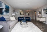Located in Ellenwood, GA, this single-floor residence offers a thoughtfully designed layout that balances comfort and modern style. The open living area is anchored by dark hardwood-style flooring, a ceiling fan, and wainscoting details along the walls. Natural light filters in through windows dressed in navy patterned curtains, complementing the contemporary furnishings and abstract wall art that carry a consistent navy and white color palette throughout the home. An adjoining dining area features a round marble-top table, mirror wall accent, and chair rail molding, creating an intimate yet refined space for entertaining. The kitchen is well-equipped with white cabinetry, quartz-style countertops, a stainless steel gas range, and a decorative tile backsplash that adds visual interest. Both bedrooms are carpeted and generously sized, offering a calm retreat. The primary bedroom includes a walk-in closet and direct access to the bathroom. The second bedroom features chevron-print curtains and ample natural light. The full bathroom is finished with wood-look flooring, a wide vanity with quartz countertop, a large mirror, and a tub-shower combination, delivering a clean, functional design that ties the home together cohesively.