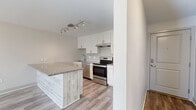 This single-floor, two-bedroom, one-bathroom unit offers a thoughtfully arranged layout that maximizes functionality within a compact footprint. The kitchen stands out with white shaker-style cabinetry, stainless steel appliances including an electric range and dishwasher, a geometric tile backsplash, and a peninsula with granite-style countertops and a wood-paneled base — providing both prep space and a casual dining area. Track lighting overhead adds a modern touch. The living area connects seamlessly to the kitchen, creating an open, practical flow.

Both bedrooms feature plush wall-to-wall carpeting, ceiling fans with light fixtures, baseboard heating, and windows with blinds that allow natural light to filter in. The primary bedroom includes two separate closets, offering generous storage. One additional room features luxury vinyl plank flooring, a wall-mounted air conditioning unit, and a baseboard heater, providing flexible climate control.

The bathroom features a full tub/shower combination finished with large white wall tiles accented by a vertical strip of decorative geometric tile in warm taupe tones, complemented by brushed nickel fixtures. A hallway connects all rooms efficiently, completing this clean, modern, and well-appointed unit.