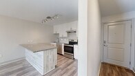 This single-floor, two-bedroom, one-bathroom unit offers a thoughtfully arranged layout that maximizes functionality within a compact footprint. The kitchen stands out with white shaker-style cabinetry, stainless steel appliances including an electric range and dishwasher, a geometric tile backsplash, and a peninsula with granite-style countertops and a wood-paneled base — providing both prep space and a casual dining area. Track lighting overhead adds a modern touch. The living area connects seamlessly to the kitchen, creating an open, practical flow.

Both bedrooms feature plush wall-to-wall carpeting, ceiling fans with light fixtures, baseboard heating, and windows with blinds that allow natural light to filter in. The primary bedroom includes two separate closets, offering generous storage. One additional room features luxury vinyl plank flooring, a wall-mounted air conditioning unit, and a baseboard heater, providing flexible climate control.

The bathroom features a full tub/shower combination finished with large white wall tiles accented by a vertical strip of decorative geometric tile in warm taupe tones, complemented by brushed nickel fixtures. A hallway connects all rooms efficiently, completing this clean, modern, and well-appointed unit.