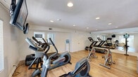 Located in El Cajon, CA, this dedicated fitness center offers a comprehensive workout environment designed to support a full range of exercise routines. The space is finished with warm, light-toned hardwood-style flooring throughout, creating a clean and inviting atmosphere that encourages activity.

The layout is thoughtfully organized across an open floor plan, divided into distinct workout zones. The cardio area is well-appointed with treadmills, elliptical trainers, a stationary spin bike, and a rowing machine, complemented by ceiling-mounted flat-screen televisions for entertainment during workouts. Multiple windows allow natural light to filter in, enhancing the bright and airy feel of the space.

The strength training section features a multi-station cable machine, weight benches, free weights, and additional resistance equipment, all positioned alongside full-length wall mirrors that help users maintain proper form. The mirrors also visually expand the space, adding to the sense of openness.

Recessed lighting throughout ensures consistent illumination at all hours. A water cooler station is conveniently placed within the room for easy hydration access. A glass-paned exterior door provides a direct connection to the outdoors, further brightening the space with natural light. Overall, this fitness center is a practical and well-maintained facility suited for diverse training needs.