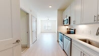 Located at 1000 Artistry Dr in Midlothian, Virginia, this single-floor residence offers a clean, modern aesthetic throughout. The open-concept layout connects the kitchen and living area seamlessly, creating a bright and airy atmosphere enhanced by light hardwood-style flooring and crisp white walls.

The kitchen is thoughtfully designed with white shaker-style cabinetry featuring brushed nickel hardware, quartz countertops, a subway tile backsplash, and a full suite of stainless steel appliances including a refrigerator, electric range, built-in microwave, and dishwasher. A stainless steel undermount sink with a brushed nickel faucet completes the functional workspace.

The living area is generously proportioned, finished with the same light hardwood-style flooring, and equipped with a ceiling fan. Natural light filters in through a window with views of the surrounding neighborhood.

The bedroom offers plush carpeting, a ceiling fan, and a window that allows ample natural light. An adjacent bathroom features large-format tile flooring, a white vanity with quartz countertop, and a walk-in closet with built-in shelving for organized storage. A stacked laundry unit is also present within the unit, adding everyday convenience to this well-appointed residence.