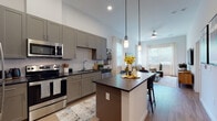 Located at 240 Grant St SE in Atlanta's Grant Park neighborhood, this single-floor residence showcases a thoughtfully designed open-concept layout with modern finishes throughout. The kitchen is a standout feature, boasting sage-gray shaker-style cabinetry, dark granite countertops, a white subway tile backsplash, and a full suite of stainless steel appliances including a refrigerator, range, microwave, and dishwasher. A central island with bar seating and sleek pendant lighting makes it ideal for both cooking and entertaining. Light wood-style flooring runs through the main living areas, seamlessly connecting the kitchen to the bright and airy living room. The living space benefits from generous natural light streaming through large windows with sheer curtains, enhanced by elevated ceilings and a ceiling fan. The bedroom offers a tranquil retreat with plush carpeting, large windows, and ample closet space. A hallway connects the bedroom to a well-finished bathroom featuring tiled walls and quality fixtures. Throughout the residence, clean white walls, recessed lighting, and contemporary design choices create a cohesive and inviting atmosphere ideal for modern urban living in Atlanta.