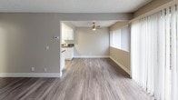 This single-story cottage is designed with a practical and comfortable layout, incorporating modern updates throughout. The living area features hard-surface flooring and a textured ceiling, with large sliding glass doors fitted with vertical blinds that fill the room with natural light and provide direct access to an outdoor area. A ceiling fan is present in the adjoining space, enhancing air circulation. The open connection between the living area and kitchen creates a cohesive flow. The kitchen is well-appointed with crisp white cabinetry, dark countertops, wood-look flooring, and stainless steel appliances including a gas range, refrigerator, and dishwasher. Flush-mount ceiling lighting keeps the kitchen bright and functional. The bedroom offers carpeted flooring for added comfort, continuing the warm and livable aesthetic found throughout the cottage. The bathroom includes wood-look flooring, a combined shower and bathtub with a curtain, and clean white fixtures with brushed nickel hardware accents. Neutral wall tones are consistent across all rooms, contributing to a cohesive and understated palette. The overall ambiance is clean, modern, and move-in ready.