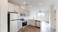 Located at 103 East 2nd Street in Richmond, VA, this thoughtfully designed one-bedroom, one-bathroom unit offers a clean, contemporary aesthetic throughout. The open-concept kitchen and living area serves as the heart of the space, featuring gray shaker-style cabinetry with matte black hardware, a white quartz peninsula with an undermount sink, and a full suite of stainless steel appliances including a refrigerator, electric range, built-in microwave, and dishwasher. A white subway tile backsplash adds a classic touch, while rich hardwood-style flooring grounds the entire living area. A large sliding glass door floods the space with natural light and provides direct access to a private balcony with views of the surrounding Richmond neighborhood. A ceiling fan in the living area adds comfort and functionality. The bedroom is carpeted for warmth and comfort, features large windows that invite abundant natural light and urban views, and is served by an adjacent closet. The bathroom continues the modern design language with gray cabinetry, a white vanity top, a large mirror, and matte black fixtures. Recessed lighting throughout maintains a bright, contemporary atmosphere.