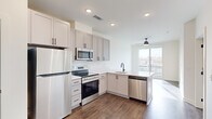 Located at 103 East 2nd Street in Richmond, VA, this thoughtfully designed one-bedroom, one-bathroom unit offers a clean, contemporary aesthetic throughout. The open-concept kitchen and living area serves as the heart of the space, featuring gray shaker-style cabinetry with matte black hardware, a white quartz peninsula with an undermount sink, and a full suite of stainless steel appliances including a refrigerator, electric range, built-in microwave, and dishwasher. A white subway tile backsplash adds a classic touch, while rich hardwood-style flooring grounds the entire living area. A large sliding glass door floods the space with natural light and provides direct access to a private balcony with views of the surrounding Richmond neighborhood. A ceiling fan in the living area adds comfort and functionality. The bedroom is carpeted for warmth and comfort, features large windows that invite abundant natural light and urban views, and is served by an adjacent closet. The bathroom continues the modern design language with gray cabinetry, a white vanity top, a large mirror, and matte black fixtures. Recessed lighting throughout maintains a bright, contemporary atmosphere.