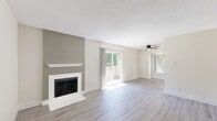 Located at 7236 Greenhaven Dr in Sacramento, CA, this two-bedroom, one-bathroom single-floor residence offers a well-organized layout designed for comfortable everyday living. The open living room is a standout space, featuring light gray luxury vinyl plank flooring, a classic fireplace set against a contrasting accent wall, a ceiling fan, and multiple windows with sliding glass door access that invite abundant natural light and outdoor views of surrounding greenery. The kitchen is thoughtfully appointed with gray shaker-style cabinetry, crisp white countertops, stainless steel appliances including a refrigerator, electric range, and dishwasher, and track lighting overhead — all set over matching light wood-tone flooring. Both bedrooms are carpeted and offer windows with views of the outdoors, providing a quiet, comfortable retreat; the primary bedroom also includes a closet. The bathroom features light wood-tone vinyl flooring, a gray vanity with a white countertop, a combined tub and shower with a glass enclosure, and clean white walls. A hallway connects the main areas efficiently. The overall aesthetic is clean and modern throughout.