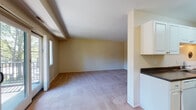 Located at 19 Thomas Olney Common in Providence, Rhode Island, this single-floor residence offers a practical and well-organized layout across a comfortable footprint. The floor plan, visible in the 3D model, reveals a logical flow between living, sleeping, and functional spaces.

The living area is generously sized, featuring neutral-toned carpet and warm beige walls. Natural light enters through sliding glass doors and large windows that provide views of the surrounding greenery, lending the space an open, airy feel. A half-wall divider separates the living area from the kitchen, maintaining visual connectivity between the two spaces.

The galley-style kitchen is efficiently designed with white cabinetry running floor to ceiling on both sides, dark granite-style countertops, wood-look flooring, and white appliances including a gas range and refrigerator. Overhead lighting keeps the space bright and functional.

Multiple carpeted bedrooms offer adequate space, each with neutral walls and windows admitting natural light. The bedrooms vary slightly in size, providing flexibility for different uses.

The bathroom includes a full tub-shower combination with tile surround, clean white fixtures, and wood-look flooring, offering a straightforward and functional design throughout.