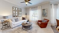 Located in Sugar Land, TX, this single-story 2-bedroom, 2-bathroom home offers a thoughtfully designed layout with modern finishes throughout. The galley-style kitchen is equipped with stainless steel appliances, white shaker cabinetry, and granite countertops, flowing into a peninsula with bar seating and pendant lighting — ideal for casual dining or entertaining. The living room features crown molding, a ceiling fan, wood-look flooring, and a large window that fills the space with natural light. The adjacent dining area continues the bright aesthetic with tall windows dressed in sheer curtains. Both bedrooms are carpeted and comfortable; the primary bedroom includes a vaulted ceiling with a ceiling fan, offering a sense of added openness. Both bathrooms are finished with marble-look tile surrounds, soaking tub-shower combos, granite vanity tops, and white cabinetry with brushed hardware. A hallway connects the rooms efficiently, keeping the layout cohesive. The overall palette is neutral and light throughout, with soft grays and whites creating a clean, modern ambiance well-suited to everyday living.