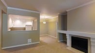 This single-floor residence offers a thoughtfully designed layout with classic architectural details that lend it a timeless appeal. The living area is anchored by a traditional fireplace with a crisp white surround and mantel, serving as a natural focal point within the room. Neutral-toned walls and light carpet flooring create a warm, inviting atmosphere throughout the space.

Crown molding runs along the ceiling edges, adding a refined finishing touch to each room. A pass-through window connects the living area to the kitchen, promoting an open and connected feel while maintaining distinct zones. The kitchen features white cabinetry and white appliances, contributing to a clean and bright aesthetic.

An adjacent dining area is illuminated by a pendant light fixture that hangs from the ceiling, adding a subtle elegance to the space. A doorway visible from the main living area hints at additional rooms beyond, suggesting a well-organized floor plan. Floor vents are integrated discreetly into the carpeted floor, ensuring functional climate control without disrupting the visual flow. Overall, the space combines classic design elements with practical layout choices to create a comfortable and cohesive living environment.