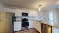 Located at 5 Captains Way in Brunswick, Maine, this single-floor residence offers a thoughtfully designed layout with a clean, contemporary aesthetic throughout. The open-concept living and dining area is anchored by durable wood-look flooring, large windows that invite abundant natural light, and baseboard heating supplemented by a wall-mounted mini-split unit for year-round comfort. A private entry door provides convenient access directly to the living space.

The kitchen is well-appointed with crisp white shaker-style cabinetry, light stone countertops, and a full suite of stainless steel appliances, including a range, over-the-range microwave, refrigerator, and dishwasher. A pendant light adds a finishing touch above the functional layout.

The bedrooms feature soft wall-to-wall carpeting, ceiling fans, and windows that bring in natural light. Generous closet space with wire shelving is included in the bedroom areas, offering practical storage solutions.

The bathroom is finished in a bright, neutral palette with light wood-look flooring, a white shaker-style vanity with brushed nickel fixtures, a wall-mounted mirror with overhead lighting, and a full soaking tub with shower. The overall design throughout the residence is clean, move-in ready, and well-suited for comfortable everyday living in the Brunswick area.