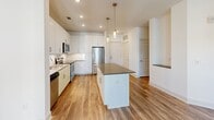 Located at 145 New Bern St in Charlotte, NC, this single-floor unit offers a well-designed, efficient layout that makes smart use of every square foot. Warm wood-look flooring flows consistently throughout the space, lending a cohesive and modern aesthetic.

The kitchen is a standout feature, equipped with sleek white cabinetry extending to the ceiling, stainless steel appliances including a refrigerator, range, and microwave, a subway tile backsplash, and a central island with a dark countertop. Pendant lighting adds a polished finishing touch above the island and counters.

The living room is bright and airy, benefiting from large windows dressed with horizontal blinds that invite ample natural light. A ceiling fan provides year-round comfort, and crisp white walls create a clean, versatile backdrop.

The bathroom is finished with light vertical subway tile surrounding a full soaking tub and shower combination, complemented by chrome fixtures and light tile flooring for a clean, contemporary feel.

A dedicated walk-in closet provides practical storage with multiple wire shelving tiers, keeping organization straightforward and accessible. The overall design of this space emphasizes clean lines, neutral tones, and functional living in a convenient Charlotte location.