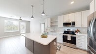 Located at 1020 E Broad St in Savannah, Georgia, this well-appointed 2-bedroom, 3-bathroom residence offers a thoughtfully designed single-floor layout with modern finishes throughout. The open-concept kitchen and living area serves as the heart of the home, featuring crisp white shaker cabinets, a hexagonal tile backsplash, quartz countertops, and a full suite of stainless steel appliances. A two-tone kitchen island with built-in shelving provides additional storage and prep space, while pendant lighting adds a polished touch overhead. Light wood-look flooring flows through the main living areas, enhancing the bright, airy feel. The living room offers direct outdoor access through a glass door, bringing in natural light and views of the surrounding greenery. Both bedrooms are carpeted for comfort and include windows fitted with white horizontal blinds. The primary bedroom features a walk-in closet with wire shelving and its own private bathroom, complete with a white vanity, quartz countertop, a large framed mirror, and wood-look flooring. The additional bathrooms maintain the same clean, contemporary aesthetic. A ceiling fan in the living area and neutral gray wall tones throughout contribute to a cohesive, modern ambiance well-suited to Savannah living.