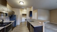 This single-floor residence offers a practical and efficiently designed layout across two bedrooms and two bathrooms. The combined kitchen and living area serves as the heart of the unit, featuring wood-style plank flooring, granite-look countertops, dark cabinetry, and stainless steel appliances including a refrigerator, electric range, and built-in microwave. A double-basin sink sits along a peninsula that helps define the space, while a pendant light illuminates the adjacent dining area, which receives natural light through a sizable window fitted with blinds. A dedicated in-unit laundry area with a washer and dryer is conveniently accessible directly from the kitchen.

Both bedrooms are carpeted and finished with neutral warm-toned walls. The primary bedroom includes a walk-in closet with double hanging rods and its own private bathroom featuring tile flooring, a shower/tub combination, and a small window for natural light. The second bathroom includes a dark-vanity with granite-style countertop and tile flooring. Each bedroom includes its own closet, and a hallway connects the private areas of the unit to the main living space.
