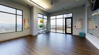 This fitness center is organized across a single floor and divided into distinct functional zones, each designed to support a comprehensive workout experience. The main exercise area features a striking blue and beige patterned rubber flooring that runs throughout, providing both durability and visual appeal. Large, wood-framed mirrors line the walls, amplifying the sense of space while allowing users to monitor their form during exercise.

The cardio zone is equipped with a row of treadmills and elliptical machines, positioned in front of the mirrored walls and illuminated by recessed linear lighting and ceiling fans that promote airflow and comfort. Adjacent to this area, the strength training section houses a variety of resistance machines, free weights, and a multi-function cable system, complemented by decorative artwork that adds a personalized touch to the environment.

A separate studio room offers a more open, flexible training space with rich hardwood flooring, floor-to-ceiling windows along one wall, and a glass-panel entry door. Natural light floods this area, providing views of the surrounding landscape. Stability balls and functional training equipment are available within this bright, airy room, making it well-suited for group classes or individual stretching and mobility work.