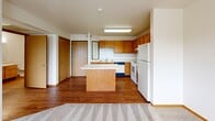 This single-floor, one-bedroom, one-bathroom unit offers a practical and well-organized layout across a compact footprint. The open-concept kitchen serves as a central hub, featuring warm honey-toned wood cabinetry that extends to the upper and lower walls, providing ample storage. A freestanding kitchen island with a light laminate countertop adds functional workspace and separates the kitchen from the adjoining living area. Standard white appliances, including a refrigerator, range, and dishwasher, are included. The kitchen transitions seamlessly into the living space, where durable hardwood-style flooring continues underfoot before giving way to neutral, patterned carpeting.

The bedroom is a well-proportioned, private room with soft carpeting, a window that allows natural light, and wood-trimmed details consistent throughout the unit. A dedicated closet provides organized storage. The bathroom is accessible via a short hallway featuring hardwood-style flooring, warm wood-toned doors, and a vanity with built-in cabinetry. A walk-in shower completes the bathroom. Throughout the unit, a textured ceiling, warm wood trim, and a neutral white palette create a clean, consistent aesthetic.