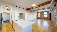 This stunning 1-bedroom, 2-bathroom apartment in Columbus, OH, showcases a perfect blend of industrial charm and modern amenities. The 1,210 sq ft space is characterized by its open-concept design, allowing for seamless flow between living areas. Exposed brick walls add character and warmth, contrasting beautifully with the sleek white surfaces throughout.

The kitchen is a highlight, featuring a large island with a white quartz countertop, stainless steel appliances, and a stylish blue-green glass tile backsplash. Modern cabinetry and under-cabinet lighting complete the contemporary look.

Hardwood floors run throughout, adding warmth and continuity to the space. Large windows flood the rooms with natural light, while exposed ductwork and pipes on the ceiling maintain the loft's industrial aesthetic. The living area is spacious and versatile, perfect for entertaining or relaxing.

The bathroom boasts a modern design with a walk-in shower, large format tiles, and a floating vanity. Thoughtful lighting, including wall sconces, adds ambiance and functionality to various areas of the apartment.

With its prime location and thoughtful design, this apartment offers a luxurious urban living experience in the heart of Columbus.