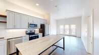 Located at 2829 SW Fairlawn Rd in Topeka, Kansas, this single-floor unit offers a thoughtfully designed open-concept layout with contemporary finishes throughout. The kitchen is a standout feature, showcasing gray shaker-style cabinetry, stone countertops, a classic white subway tile backsplash, and stainless steel appliances including a range, microwave, dishwasher, and refrigerator. Warm-toned open wood shelving adds a rustic contrast to the clean, modern aesthetic. A large island with a stone surface provides additional workspace and casual dining space. The kitchen flows seamlessly into the living area, which is bathed in natural light from French doors that open to a balcony with outdoor views. Light wood-style flooring runs throughout the main living spaces, enhancing the bright and airy ambiance. The bedrooms are carpeted for comfort and feature ceiling fans and windows with roller shades. The bathrooms are finished with stone countertops, undermount sinks, brushed gold fixtures, and large mirrors. Recessed lighting throughout the unit adds to the clean, polished interior. The overall design balances modern functionality with warm, inviting details.