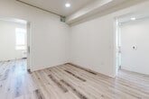 This thoughtfully designed single-floor unit offers a clean, modern aesthetic defined by an all-white palette, light wood-tone flooring, and recessed lighting throughout. The open layout maximizes the available floor area, creating a cohesive flow between the living and sleeping spaces.

The kitchen is outfitted with flat-front white lower cabinetry paired with contrasting grey upper cabinets, a sleek countertop with an undermount sink, a built-in oven, an induction cooktop, and a full-size refrigerator — delivering a fully functional and visually streamlined cooking space.

The sleeping area features frosted glass sliding barn-style doors, offering privacy while maintaining the unit's bright and airy feel. Built-in shelving and closet systems with dedicated drawer units provide generous, well-organized storage. A secondary room or flex space includes additional built-in open shelving, suited for a home office or storage use.

The bathroom is clean and functional, featuring a wall-mounted toilet, a soaking tub with a tiled surround, grab bars, and matching wood-tone flooring. Throughout the unit, natural light filters in through well-placed windows, with city views visible from the bedroom, reinforcing the elevated and contemporary character of this efficiently designed space.