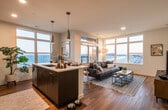 This single-floor residence is defined by its open-concept design and remarkable panoramic views of the ocean and boardwalk, visible through expansive floor-to-ceiling windows and large multi-pane windows throughout the living areas. Natural light floods the space, enhancing the warm, light-toned hardwood flooring that runs through the main living areas.

The kitchen is a standout feature, outfitted with rich dark espresso cabinetry extending to the ceiling, stainless steel appliances including a refrigerator, microwave, and range, and a white quartz countertop with a subway tile backsplash. A central island with seating serves as both a functional workspace and a casual dining area, with pendant lighting overhead.

The living room opens directly from the kitchen, offering an inviting and spacious area anchored by large windows framing dramatic coastal views. A secondary sitting area provides additional flexible living space.

The bedrooms are quiet and comfortable, carpeted for warmth, each featuring generous windows with city or skyline views and ample natural light. Bathrooms are finished with neutral tile flooring, dark vanity cabinetry, and clean white fixtures, including a full tub-shower combination in one bathroom.