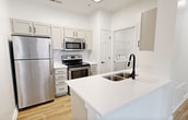 This 590-square-foot, one-bedroom, one-bathroom apartment at 2031–2055 Ovaltine Ct in Villa Park, IL is thoughtfully designed to maximize space and functionality across a single floor. The open-concept living room and kitchen area is anchored by light hardwood-style flooring and crown molding, with a ceiling fan overhead providing comfort year-round. Sliding glass doors with vertical blinds lead to a private balcony overlooking lush greenery, while an additional window fills the space with abundant natural light. The kitchen features white shaker cabinets, a subway tile backsplash, white countertops with a peninsula island, a double-basin sink with a matte black faucet, and a full suite of stainless steel appliances including a refrigerator, electric range, and over-the-range microwave. In-unit laundry hookups are conveniently located just off the kitchen. The 140-square-foot bedroom offers plush carpeting, a ceiling fan, a natural light-filled window, and access to both a closet and the hallway. The bathroom is finished with marble-style tile surrounding the tub/shower combo, complemented by matte black fixtures and a clean white vanity with hardwood-style flooring.