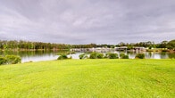 Located at 6300 Moseley Dixon Rd in Macon, Georgia, this waterfront property offers a compelling combination of open green space and direct lake access. The grounds are characterized by gently rolling, well-maintained lawns that slope naturally down toward the water's edge, creating a seamless transition between the landscaped terrain and the calm, reflective surface of the lake. Mature trees are thoughtfully positioned throughout the property, providing natural shade and visual interest while complementing the open character of the grounds.

The lakefront setting is a standout feature, with unobstructed views across the water to densely wooded, pine-lined shores on the opposite bank. The shoreline is bordered by native shrubs and vegetation, reinforcing the property's natural aesthetic. A multi-story residential building with balconies is situated on the upper portion of the grounds, taking full advantage of the elevated vantage point and panoramic water views.

Additional structures and landscaped areas are visible across the broader site, including paved pathways, ornamental plantings, and open lawn areas suited for a variety of uses. The overall ambiance is peaceful and scenic, defined by the interplay of open sky, lush greenery, and tranquil lake water — making this a distinctive waterfront property in the Macon, Georgia area.