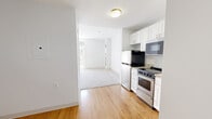 Located at 873 Harwich Road in Brewster, Massachusetts, this efficiently designed single-floor unit offers a thoughtful layout across three distinct areas. The kitchen is a standout feature, equipped with white shaker-style cabinetry, granite countertops, stainless steel appliances including a range, over-the-range microwave, and refrigerator, all set atop warm hardwood flooring. The open sightline from the kitchen into the living area creates a sense of connectivity throughout the space. The living area is generously proportioned for the footprint, finished with plush wall-to-wall carpeting that adds comfort underfoot. A set of classic French doors with transom window above floods the room with natural light and provides views of the surrounding greenery, enhancing the bright, airy atmosphere. A double-door closet in the living area offers practical storage. The bathroom is clean and functional, featuring a white vanity with granite countertop, a wall-mounted mirror with overhead lighting, hardwood flooring, and an accessible roll-in shower with grab bars. The unit's neutral white walls and consistent finishes throughout create a cohesive, move-in-ready environment suited for comfortable everyday living in a Cape Cod setting.