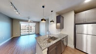 This thoughtfully designed one-bedroom, one-bathroom unit offers an efficient and stylish single-floor layout. The open-concept living and kitchen area serves as the heart of the space, featuring warm hardwood-style flooring, recessed lighting, and sleek pendant lights above a central kitchen island. The island is topped with granite countertops and includes a stainless steel sink, complementing the full suite of stainless steel appliances — including a refrigerator, range, microwave, and dishwasher. Dark espresso-toned cabinetry with a subway tile backsplash adds a modern contrast throughout the kitchen. The living area flows naturally toward a sliding glass door that opens to a private balcony, allowing ample natural light and outdoor views. A ceiling fan overhead enhances comfort in this shared living space. The bedroom offers plush carpeting, a large window with exterior views, and convenient direct access to both the full bathroom and a dedicated closet. The bathroom features granite countertops, a bold navy vanity cabinet, a large mirror, and hardwood-style flooring that ties the space together. Clean neutral tones and modern fixtures throughout create a cohesive, contemporary ambiance.