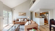 This well-appointed two-story home offers a thoughtfully designed layout spread across two floors. The main level is the larger of the two and serves as the heart of the home, featuring an open-concept living, dining, and kitchen area. The living room immediately impresses with dramatic vaulted ceilings that rise to a striking height, a tile-surround fireplace as a focal point, and sliding glass doors that invite an abundance of natural light. Light wood-tone flooring runs throughout the main level, contributing to a bright and cohesive atmosphere. The kitchen features warm wood cabinetry, light countertops, and a breakfast bar that opens seamlessly to the dining area. The dining space is anchored by a ceiling fan light fixture and sits adjacent to a staircase leading to the upper floor. Upstairs, the private bedroom offers plush carpeting, a large window with outdoor views, and direct access to a dedicated walk-in closet. The full bathroom is finished with a light countertop vanity, a wide mirror, and neutral tiling. A separate closet provides additional storage on the upper level. The home's two-story design, vaulted ceilings, and open main floor create a sense of spaciousness that extends well beyond its footprint.