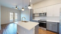 This 550 square foot apartment in Austin, TX, offers a thoughtfully designed living space that maximizes functionality and style. The single-floor layout comprises one bedroom, one bathroom, a kitchen, and a closet. The primary bedroom, measuring 110 square feet, provides a comfortable retreat with a large window allowing natural light to flood the space.

The kitchen is a standout feature, boasting a contemporary design with two-tone cabinetry in white and blue-gray. A central island with a built-in sink and sleek white countertops offers additional workspace and casual dining. Stainless steel appliances, including a refrigerator with water dispenser and built-in microwave, complete the modern aesthetic.

The bathroom showcases a clean, minimalist design with a glass-enclosed shower, white fixtures, and a gray vanity with ample storage. The warm wood-look flooring flows throughout the apartment, creating a cohesive and inviting atmosphere. Recessed lighting and pendant fixtures provide layered illumination, enhancing the overall ambiance.

Large windows in both the bedroom and living area not only bring in abundant natural light but also offer views of the surrounding greenery. The neutral color palette, dominated by whites and grays, lends a fresh and airy feel to the space, making it appear larger than its actual square footage.