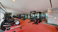 Located at 511 Fayetteville St in the heart of Raleigh, NC, this fitness center offers a comprehensive and thoughtfully designed workout environment across a single floor. The space is anchored by bold red sport flooring throughout the main exercise area, immediately establishing an energetic atmosphere suited for serious training.

The strength training zone is generously outfitted with a power rack system, cable machines, a full dumbbell rack, adjustable benches, and battle ropes, providing options for a wide range of resistance training exercises. Large floor-to-ceiling mirrors line the walls, amplifying the sense of space and allowing users to monitor their form throughout their workouts. A distinctive circuit-board-inspired accent wall adds a modern, urban aesthetic to the interior design.

The cardio area benefits from an abundance of natural light streaming through expansive floor-to-ceiling windows that overlook an outdoor pool and terrace. Cardio equipment includes treadmills, ellipticals, stationary bikes, and a rowing machine, all positioned to take advantage of the bright, open views. Mounted televisions are placed throughout the facility for entertainment during workouts.

The entry area features a clean, welcoming corridor with built-in wood cubbies for storing personal items, as well as a large window offering a preview into the fitness floor beyond. Recessed lighting throughout contributes to a well-lit, polished environment that is both functional and visually appealing.
