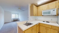 This single-story two-bedroom, one-bathroom unit in Clayton, California offers a clean, functional layout designed for comfortable everyday living. The open-concept kitchen flows directly into the living area, creating a connected and practical space. The kitchen is outfitted with light oak cabinetry providing ample upper and lower storage, white appliances including a refrigerator, electric cooktop, and microwave, along with light-toned countertops and a stainless steel sink set into a peninsula that separates the kitchen from the living room. The living area features neutral carpet flooring, a ceiling fan, and a window with an in-wall HVAC unit that allows for individual climate control.

A carpeted hallway connects the two generously sized bedrooms, each featuring neutral carpet, white walls, and windows offering outdoor views and natural light. The full bathroom is designed with accessibility in mind, including multiple stainless steel grab bars near the toilet and bathtub, tile flooring, and a tub-shower combination. The unit maintains a bright, neutral palette throughout, with white walls and consistent flooring materials that create a cohesive and move-in ready environment.