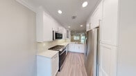 Located at Fairfield Townhouses in Bohemia, NY, this multi-level townhouse spans three floors and showcases a thoughtfully designed interior with consistent, modern finishes throughout. The entry foyer welcomes residents with light hardwood-style flooring, crisp crown molding, recessed lighting, and a built-in security system panel, setting the tone for the rest of the home.

The kitchen is a standout feature, offering white shaker-style cabinetry, stone countertops, a marble-style tile backsplash, and stainless steel appliances including a gas range, built-in microwave, and French door refrigerator. A double sink sits beneath a window, allowing natural light to fill the space.

Adjacent to the kitchen, the dining area is brightened by a large window with outdoor views and is accented by a classic chandelier. The living area features sliding glass doors leading to an outdoor space, along with additional windows that bring in generous natural light. Ceiling fans provide comfort in the main living spaces.

The bathrooms are finished with subway tile wainscoting, mosaic tile flooring, and marble-topped vanities, lending a clean and refined aesthetic. The attached garage features a painted concrete floor, built-in shelving, and direct interior access, offering practical storage and parking convenience.