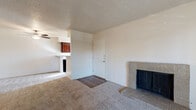 This single-floor residence offers a well-organized layout with distinct living, sleeping, kitchen, and bathroom areas. The living room serves as the central gathering space, finished with plush carpeting, a textured ceiling, and a sliding glass door that invites natural light while providing access to an outdoor area with exterior views. A standout feature of the living room is the brick-surround fireplace with metal doors, adding a classic and functional focal point to the space. A dedicated entryway with hardwood-style flooring transitions seamlessly from the front door into the carpeted living area. The galley-style kitchen is efficiently designed with rich dark wood cabinetry on both sides, light countertops, a double sink, and black appliances including a refrigerator, stove, and over-the-range microwave. A window at the end of the kitchen allows additional natural light to filter through. The bedrooms are generously sized, each carpeted and featuring large windows that bring in ample daylight and views of the surrounding neighborhood. The primary bedroom includes direct access to a private bathroom and a walk-in closet area. Bathrooms are finished with white square tile surrounding a full soaking tub, wood-style flooring, and dark vanity cabinetry, offering a clean and functional design throughout.