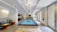 Located at 425 N Boylan Avenue in Raleigh, NC, this single-floor community amenity space offers a well-appointed and thoughtfully designed gathering area for residents. The open layout is anchored by a striking coffered ceiling with geometric detailing and an elegant chandelier, lending the space a refined yet welcoming ambiance.

At the center of the room, a full-size billiards table serves as a focal point, positioned beneath the decorative ceiling treatment. Adjacent to it, a live-edge wood communal table surrounded by patterned accent chairs provides a casual dining and social area. The kitchenette runs along one wall and features rich wood cabinetry, stainless steel appliances including a dishwasher and refrigerators, a mosaic tile backsplash, and mirrored upper panels that enhance the sense of depth.

A cozy lounge area anchored by a stacked stone accent wall houses a modern fireplace and wall-mounted television, with teal upholstered chairs and colorful accent pillows creating a warm and inviting retreat. Large floor-to-ceiling glass doors and windows flood the space with natural light and offer direct views and access to an outdoor pool and courtyard area.

A small business nook near the entrance provides a workstation with a desktop computer, offering functional utility. Light tile flooring and crisp white walls unify the space throughout.
