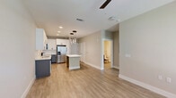 Located in Sanford, FL, this thoughtfully designed one-bedroom, one-bathroom unit offers a comfortable and modern living experience across a single floor. The open-concept kitchen and living area serves as the heart of the home, showcasing light wood-look flooring, recessed lighting, and a striking set of pendant lights above a central island with a clean white countertop. The kitchen features white upper cabinetry, gray lower cabinetry with matte black hardware, stainless steel appliances, and ample storage throughout. The adjacent living space is bright and airy, with natural light streaming in through windows fitted with blinds and a door providing additional access and light. The bedroom is a well-sized, serene retreat with plush carpeting, a ceiling fan, and a window overlooking the outdoors. A dedicated closet adds practical storage. The bathroom is finished to a high standard, featuring a gray vanity with a white countertop, a large framed mirror, stylish wall sconces, and a glass-enclosed walk-in shower with marble-style tile surrounds. Throughout the unit, neutral tones and modern fixtures create a cohesive, clean aesthetic. The exterior is part of a multi-story building with a well-maintained landscape.