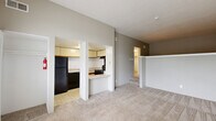 Located at 2975 Coast Dr in Indianapolis, IN, this single-floor unit offers a well-organized layout comprising a living room, kitchen, bathroom, and closet. The living room is a bright, welcoming space anchored by tall windows fitted with horizontal blinds that allow generous natural light to fill the room. Soft, neutral-toned carpeting runs throughout the living areas, contributing to a warm and cohesive atmosphere. A white entry door with a window panel provides additional light and direct access to the outdoors. The kitchen is efficiently designed with cream-colored cabinetry, a light countertop surface, and a breakfast bar peninsula that opens toward the living room. Black appliances — including a refrigerator, electric range, and dishwasher — are included, along with an under-cabinet range hood and a single-basin sink. Tile flooring in the kitchen offers a practical contrast to the carpeted living spaces. The bathroom features a full tub-and-shower combination with white tile surround, chrome fixtures, and tile flooring, maintaining a clean and functional aesthetic. A dedicated closet provides convenient storage. The overall design is straightforward and functional, with neutral wall tones and consistent finishes throughout.