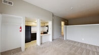 Located at 2975 Coast Dr in Indianapolis, IN, this single-floor unit offers a well-organized layout comprising a living room, kitchen, bathroom, and closet. The living room is a bright, welcoming space anchored by tall windows fitted with horizontal blinds that allow generous natural light to fill the room. Soft, neutral-toned carpeting runs throughout the living areas, contributing to a warm and cohesive atmosphere. A white entry door with a window panel provides additional light and direct access to the outdoors. The kitchen is efficiently designed with cream-colored cabinetry, a light countertop surface, and a breakfast bar peninsula that opens toward the living room. Black appliances — including a refrigerator, electric range, and dishwasher — are included, along with an under-cabinet range hood and a single-basin sink. Tile flooring in the kitchen offers a practical contrast to the carpeted living spaces. The bathroom features a full tub-and-shower combination with white tile surround, chrome fixtures, and tile flooring, maintaining a clean and functional aesthetic. A dedicated closet provides convenient storage. The overall design is straightforward and functional, with neutral wall tones and consistent finishes throughout.