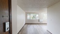 Located at 1900 Naval Ave in Bremerton, Washington, this single-floor, one-bedroom, one-bathroom unit offers a well-organized and efficient layout. Light vinyl plank flooring flows throughout, complemented by textured ceilings and neutral walls that create a clean, bright atmosphere.

The living room is the most spacious area of the unit, featuring multiple windows that frame views of surrounding greenery, allowing generous natural light to fill the room. A wall-mounted heater provides practical climate control. The adjoining dining area transitions smoothly from the living space, enhancing the open feel of the main living zone.

The kitchen is thoughtfully arranged with white cabinetry, granite-style countertops, a full-size refrigerator, a range, and a sink with ample counter space on both sides — offering solid functionality within a compact footprint.

The bedroom is a comfortable, well-proportioned room with a window overlooking outdoor greenery and a baseboard heater. Rich dark-wood-trimmed doors lead to two closets, providing notable storage for the unit's size. The closets feature built-in shelving and hanging rods for organized storage.

The bathroom includes a vanity with granite-style countertops, cabinetry below, and a mirror, rounding out the practical and consistent design found throughout this tidy Bremerton residence.