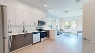 Located at 345 Lincoln Ave in Amherst, MA, this single-floor unit offers a thoughtfully designed layout that maximizes its compact footprint. The open-plan kitchen and living area form the heart of the space, finished throughout with light hardwood-style flooring that enhances the bright, airy atmosphere.

The kitchen is outfitted with a two-tone cabinet scheme—white upper cabinets contrasting with dark wood-grain lower cabinets—accented by matte black hardware. Stainless steel appliances include a full-size refrigerator, electric range, microwave, and dishwasher, complemented by white quartz countertops and a single-basin sink with a sleek black faucet. A peninsula with seating provides a natural transition into the living area.

The living area receives ample natural light through large windows framing views of surrounding greenery, creating a calm, inviting atmosphere. Recessed and pendant lighting provide well-distributed illumination throughout.

A hallway connects to the bathroom, which features a wood-grain vanity with white countertop, a walk-in shower, and coordinating light hardwood-style flooring. Clean white walls and minimalist finishes are consistent throughout, giving the entire space a cohesive, contemporary character.
