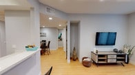 Located at 7139 Woodley Ave in the Van Nuys neighborhood of Los Angeles, this single-floor residence offers a thoughtfully designed layout with consistent light wood flooring and a neutral gray-and-white color palette throughout. The open-concept living area is anchored by a wall-mounted television and a sliding glass door fitted with vertical blinds, allowing natural light to fill the space and providing outdoor access. The kitchen is equipped with rich dark wood cabinetry featuring a high-gloss finish, white countertops, and stainless steel appliances including a gas range and built-in microwave. A dedicated dining area with recessed lighting comfortably accommodates a round glass table with seating for four. The primary bedroom offers a serene retreat with warm neutral tones and hardwood-style flooring, while the second bedroom features a mirrored sliding closet door and ample natural light. The bathroom includes a combination tub and shower with floor-to-ceiling travertine-style tile and a glass enclosure. Recessed lighting is featured throughout, and the space benefits from a clean, modern aesthetic that flows seamlessly from room to room.