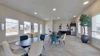 This single-floor community clubhouse offers a generously sized, open-concept layout designed to accommodate a variety of social activities. The space is finished with light wood-look tile flooring throughout, complementing the neutral, warm-toned walls and recessed lighting that create a bright, welcoming ambiance.

Upon entry, a glass-paneled door leads into a foyer area with direct outdoor views, setting a transparent and airy tone. The main gathering area features multiple seating arrangements, including round tables paired with a mix of teal and cream upholstered chairs, encouraging both casual conversation and group dining. A row of large windows lines the perimeter, flooding the interior with natural light and offering views of the surrounding neighborhood.

At the rear of the space, a well-equipped kitchenette features dark espresso cabinetry, granite countertops, a double sink, microwave, and a stainless steel refrigerator with a water dispenser, accented by floating shelves and modern pendant lighting. A dedicated lounge and game area includes a billiard table, comfortable seating, and decorative artwork, adding a recreational dimension. The overall design balances functionality with a modern, community-focused aesthetic.