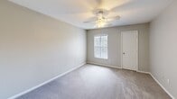 Located at 1355 Bradley Blvd in Savannah, Georgia, this two-story home offers a well-organized layout across two floors, with the majority of the living space situated on the upper level. The entry level leads to a carpeted staircase with a white handrail, guiding residents up to the main living area. The upper floor opens to a spacious living area featuring soft, neutral-toned carpet, a ceiling fan with a light fixture, and windows dressed with vertical blinds that allow natural light to fill the room. The kitchen is thoughtfully designed with warm wood-toned cabinetry, stainless steel appliances including a refrigerator, range, and microwave, and a peninsula counter with an integrated sink that separates the kitchen from the living space. Wood-style flooring grounds the kitchen area. The generously sized primary bedroom is carpeted and includes a ceiling fan, a window with vertical blinds, and access to a dedicated closet. The full bathroom features a single-sink vanity with wood cabinetry, a large mirror, tiled tub-shower combination, and wood-style flooring. A dedicated laundry room houses a full-size washer and dryer. Throughout the home, clean white walls, neutral tones, and practical finishes create a comfortable, functional living environment.