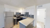 This single-floor space showcases a thoughtfully designed, modern interior that prioritizes both functionality and contemporary aesthetics. The kitchen serves as a standout feature, boasting crisp white upper cabinetry paired with sleek, dark lower cabinets for a striking two-tone contrast. A generous quartz countertop peninsula provides ample workspace and doubles as a casual dining or gathering area. The full suite of stainless steel appliances — including a refrigerator, electric range, and over-the-range microwave — adds a polished, professional feel to the space. A classic slate-blue subway tile backsplash runs the length of the cooking and prep area, introducing a subtle pop of color that complements the neutral palette throughout. Track lighting above the workspace ensures excellent task illumination, while a window allows natural light to filter in, brightening the area. The light-toned hardwood flooring flows seamlessly through the space, contributing to an open and airy ambiance. A textured ceiling adds a layer of classic character. Overall, this space combines clean lines, modern finishes, and practical design to create a welcoming and highly functional environment.