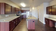 This single-floor residence offers a thoughtfully designed layout that balances comfort and functionality throughout. The open-concept kitchen serves as a central highlight, showcasing rich dark-stained cabinetry, granite countertops, and a full suite of stainless steel appliances including a range, over-the-range microwave, and refrigerator. A kitchen island with a built-in sink and pendant lighting adds both workspace and style, while dark hardwood-style flooring anchors the area with warmth.

The spacious living area features the same hardwood-style flooring, neutral gray walls, a textured ceiling, and generous windows with vertical blinds that invite natural light. Each bedroom is carpeted for comfort, with large windows offering outdoor views and baseboard heating for year-round climate control. One bedroom includes a wall-mounted AC unit for added comfort.

The full bathroom is finished with the same granite countertops and dark cabinetry found in the kitchen, paired with a tub-shower combination and hardwood-style flooring. A dedicated walk-in closet with wire shelving and rod systems provides ample storage, while a separate in-unit laundry area accommodates a full-sized washer and dryer side by side, topped with an additional storage shelf.