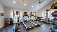 Located at 4982 S Ulster St in Denver, CO, this fitness center is a comprehensive, single-floor facility designed to support a wide range of workout routines. The space is divided into distinct functional zones, each thoughtfully appointed with quality equipment.

The cardio area features multiple treadmills and elliptical machines, each equipped with individual monitors, alongside a stationary spin bike and a rowing machine. A ceiling fan and recessed lighting keep the area comfortable and well-lit, while windows with blinds invite natural light and outdoor views.

The strength training zone is equally well-stocked, housing a cable crossover machine, a full rack of dumbbells, kettlebells, medicine balls, plyo boxes, and a power tower for bodyweight exercises. A large wall-mounted mirror amplifies the sense of space and allows for form checks during workouts.

A dedicated functional training area features TRX suspension straps mounted to a wall-mounted rig, alongside posted instructional guides. This zone transitions into a light-filled open area with wood-look flooring, offering space for stretching, yoga, or mat-based exercises. A yoga mat and stability ball are also on hand.

Natural light flows throughout the facility via large windows and a glass-panel entry door. The vaulted ceilings in the main workout area add an open, airy ambiance, making this fitness center a well-rounded and inviting space for residents.