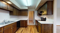 Located at 400 E Alexandersville-Bellbrook Rd in Centerville, Ohio, this single-floor property offers a practical and functional layout across several well-defined living spaces. The galley-style kitchen is outfitted with dark walnut-toned cabinetry lining both walls, white countertops, black appliances including an electric range and dishwasher, and durable hardwood-style flooring. A dedicated laundry area with a stacked washer and dryer unit adjoins the kitchen, adding everyday convenience. The living room serves as a central gathering space, highlighted by a full brick fireplace with a wood mantel and a ceiling fan overhead, all set atop neutral carpeting. A separate dining area features a chandelier light fixture. The bedrooms are carpeted and well-lit by natural light through multiple windows, with one bedroom offering dual closets for generous storage. Two full bathrooms are present: one features white subway tile wainscoting, a tiled floor, and a single vanity, while the second includes a tub-shower combination and a vanity with a colored sink. Baseboard heating units are found throughout, and the overall layout, as visible in the floor plan, provides a spacious and well-connected flow between rooms.