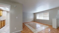 This single-floor home offers a practical and functional layout across several well-defined living spaces. The living area features a distinctive two-tone tile floor with a decorative inlay pattern of cream and terracotta tiles, complemented by neutral gray walls and a window that allows natural light to fill the room. A built-in shelving unit divides the living space from the adjoining area, which continues the warm terracotta tile flooring throughout.

The galley-style kitchen is efficiently designed with warm wood cabinetry lining both walls, granite-look countertops, a stainless steel sink, and a patterned tile backsplash. White appliances, including a refrigerator and electric range, are neatly integrated, while decorative patterned floor tiles add visual interest underfoot. A skylight overhead brightens the space naturally.

The bedrooms feature neutral tile flooring and ceiling fans with light fixtures, with one bedroom offering a window with outdoor views and another providing generous closet storage with bifold doors. Both bathrooms are consistently appointed, featuring rich dark wood vanities with cream countertops, framed mirrors, tile flooring, and walk-in shower areas. The overall ambiance throughout the home is clean, neutral, and move-in ready.