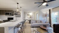 This thoughtfully designed single-floor residence offers a seamless blend of modern style and everyday functionality. The open-concept layout connects the kitchen, dining, and living areas into one cohesive, light-filled space. The kitchen is outfitted with gray shaker-style cabinetry, white quartz countertops, stainless steel appliances, and a classic subway tile backsplash. A peninsula with bar seating and elegant pendant lighting adds a stylish focal point and encourages casual dining. The dining area flows naturally into the living room, where large windows dressed with layered curtains invite abundant natural light. Ceiling fans are present throughout, enhancing comfort in the main living areas and bedroom. Light wood-style flooring runs throughout the common areas, adding warmth and continuity. The bedroom features plush carpeting, generous natural light through a bright window, and a ceiling fan overhead. The bathroom is clean and functional, featuring a sliding glass walk-in shower, gray cabinetry, and wood-look flooring. A dedicated in-unit laundry room with a full-size washer and dryer adds exceptional convenience. The overall aesthetic is contemporary and cohesive, with neutral tones and modern finishes creating an inviting, move-in-ready atmosphere.